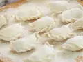 Surowe pierogi, gotowe do gotowania, posypane mąką. Wyglądają jak najlepsze ciasto na pierogi, które mama kiedyś robiła.