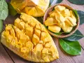 Chlebowiec właściwości: soczyste, żółte segmenty owocu jackfruit, częściowo wyjęte z łupiny i ułożone w koszyku, otoczone zielonymi liśćmi.