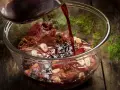 Ciemny płyn wlewa się do szklanej miski z karczkiem, czosnkiem i ziołami. Powstaje aromatyczna marynata do karczku.