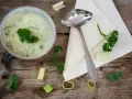 Kremowy sos porowy z natką pietruszki, podany w misce, obok łyżki i kawałków pora.