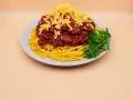 Prosty przepis na spaghetti z mięsem mielonym: makaron, sos boloński, starty ser i natka pietruszki na talerzu.