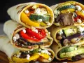 Pyszna tortilla z airfryer wypełniona grillowanymi warzywami: cukinią, papryką, bakłażanem i grzybami, posypana fetą.