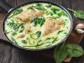 Soczysta pierś z kurczaka ze szpinakiem w sosie śmietanowym, podana w patelni. Aromatyczny czosnek i świeże liście szpinaku dopełniają danie.
