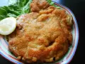 Złocisty kotlet schabowy Magdy Gessler, podany z liściem sałaty i plasterkiem cytryny na kolorowym talerzu.