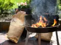 Rozpalony grill z płomieniami i dymem, obok torba z węglem. Idealny początek, by dowiedzieć się, jak rozpalić grilla.