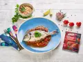 Dorada ryba w sosie pomidorowo-fasolowym, udekorowana kolendrą. Obok miseczka fasoli, czosnek, limonka i pomidorki.