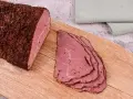 Kawałek pastrami, co to jest? Aromatyczne, peklowane i wędzone mięso wołowe, pokrojone w cienkie plastry, leży na desce.