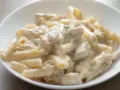 Penne z kurczakiem w kremowym sosie śmietanowo-serowym, udekorowane gałązką ziół. Pyszne danie obiadowe.
