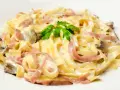 Tagliatelle z szynką i pieczarkami w kremowym sosie, z dodatkiem mozzarelli. Udekorowane natką pietruszki.