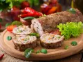 Pokrojone zrazy z mięsa mielonego z warzywami na desce, obok sałata, pomidory i papryczki chili.