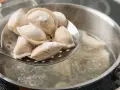 Gotowanie pierogów: na łyżce cedzakowej świeżo uformowane pierogi czekają na wrzucenie do wrzątku.