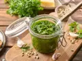 Słoik domowego pesto z pietruszki, z czosnkiem, nasionami słonecznika i serem w tle. Idealne do makaronu lub na grzanki.