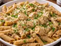 Pyszne danie z makaronem pełnoziarnistym penne, kawałkami kurczaka i parmezanem, posypane świeżą natką pietruszki.