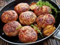 Usmażone kotlety na burgera z cebulą i ziołami na patelni.