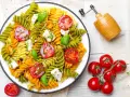 Kolorowy makaron z zielonego groszku, pomidorkami koktajlowymi i fetą, polany pesto.