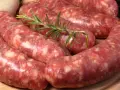 Salsiccia co to? Surowe kiełbaski wieprzowe, przyprawione ziołami, leżą na desce.