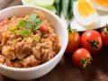Pyszna pasta z makreli w pomidorach, udekorowana szczypiorkiem i natką. Obok świeże pomidorki i jajka na twardo.