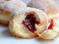 Pączki z dżemem posypane cukrem pudrem, jeden nadgryziony.