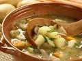 Gęsta zupa ziemniaczana z grzybami i marchewką, jak z przepisu babci. Drewniana łyżka zanurzona w aromatycznym bulionie.