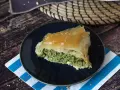 Kawałek spanakopity z chrupiącym ciastem filo i zielonym nadzieniem ze szpinaku i sera feta, posypany sezamem.