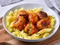 Pulpety w sosie pomidorowym jak u babci, podane z makaronem fusilli. Danie ozdobione posiekaną natką pietruszki.