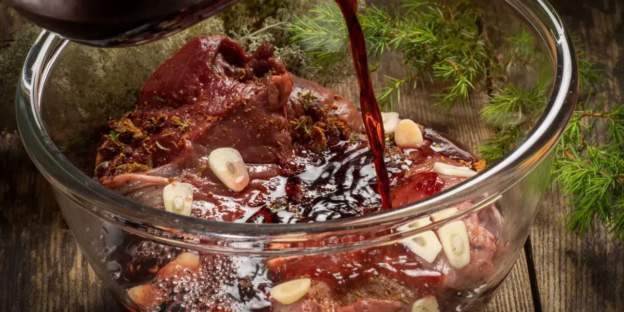 Ciemny płyn wlewa się do szklanej miski z karczkiem, czosnkiem i ziołami. Powstaje aromatyczna marynata do karczku.