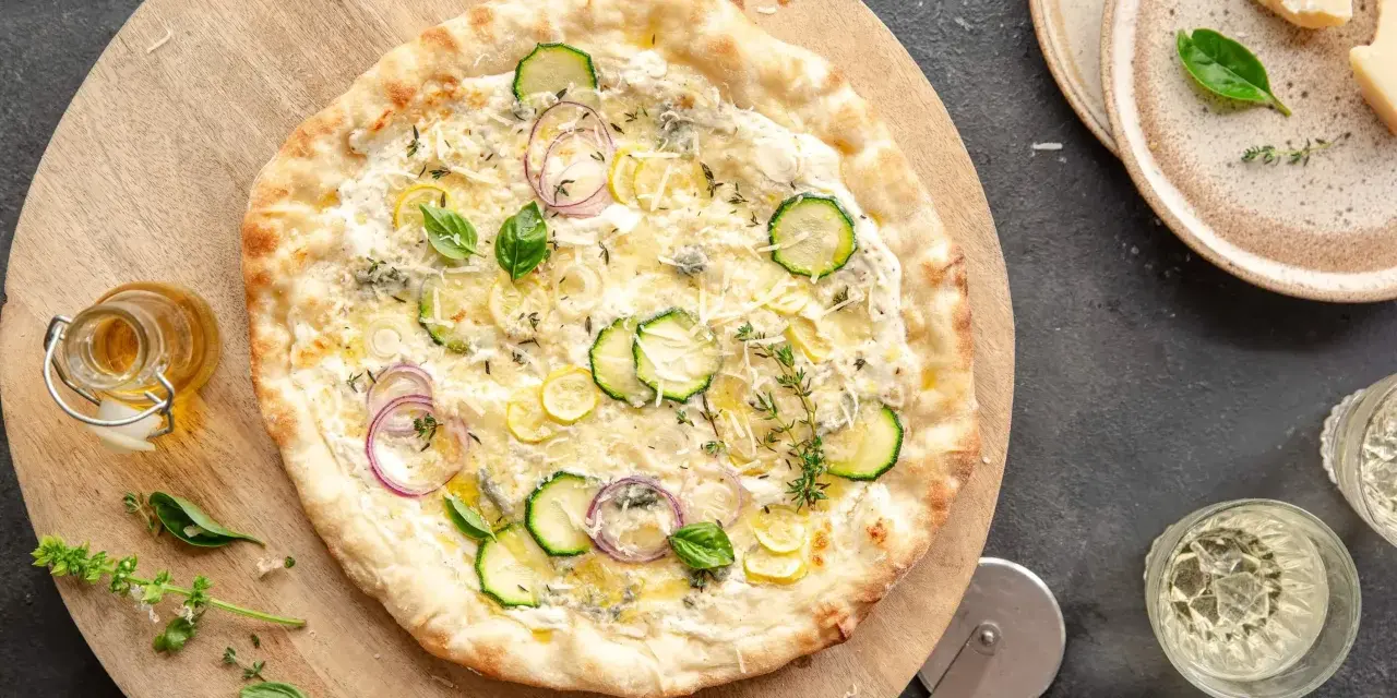 Pyszna pizza bianca z cukinią, cebulą i cytryną, ozdobiona bazylią i tymiankiem. Idealna na letni wieczór.