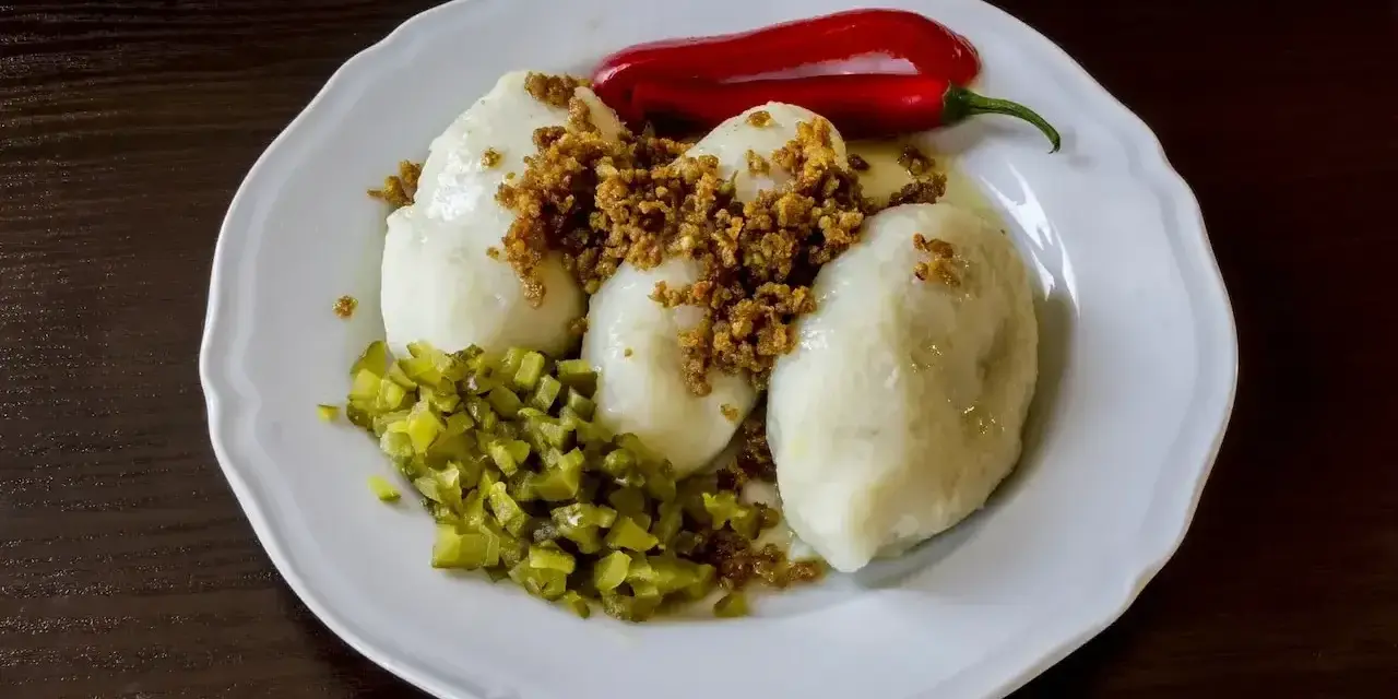 Trzy ziemniaczane kartacze z okrasą, posypane skwarkami, podane z ogórkiem kiszonym i papryczką chili.
