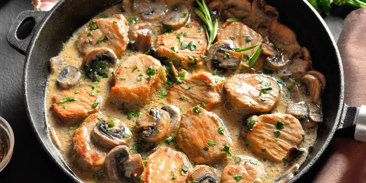 Soczysty schab w sosie pieczarkowym, udekorowany natką pietruszki, podany w żeliwnej patelni. Aromatyczne danie, które zachwyca smakiem.