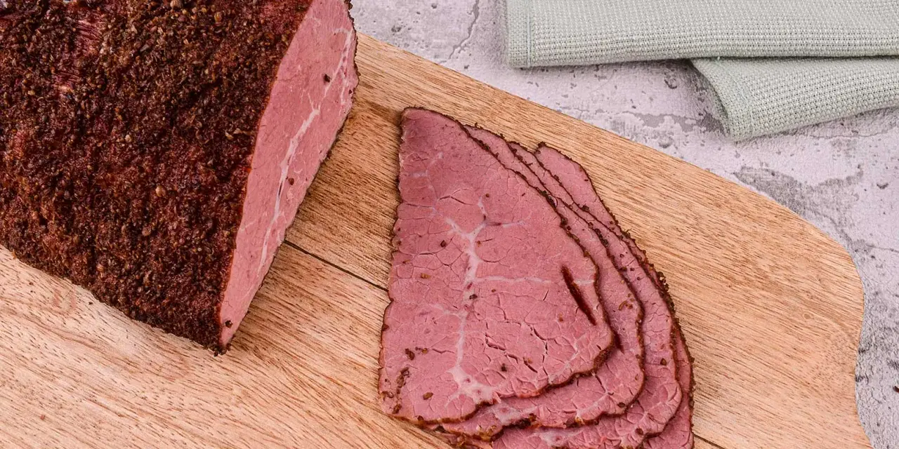 Kawałek pastrami, co to jest? Aromatyczne, peklowane i wędzone mięso wołowe, pokrojone w cienkie plastry, leży na desce.