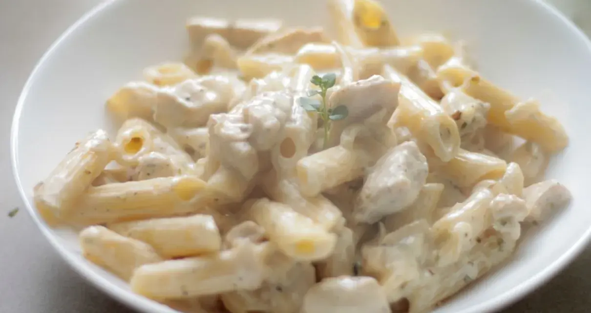 Penne z kurczakiem w kremowym sosie śmietanowo-serowym, udekorowane gałązką ziół. Pyszne danie obiadowe.