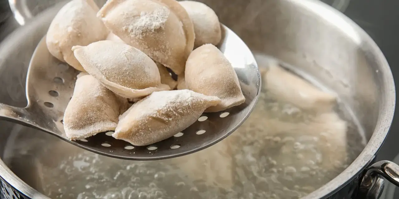 Gotowanie pierogów: na łyżce cedzakowej świeżo uformowane pierogi czekają na wrzucenie do wrzątku.