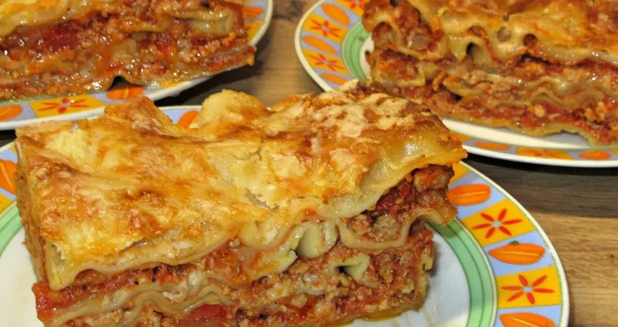 Prosty przepis na lasagne z mięsem mielonym. Aromatyczne, warstwowe danie z makaronem, sosem mięsnym i serem, podane na kolorowych talerzach.