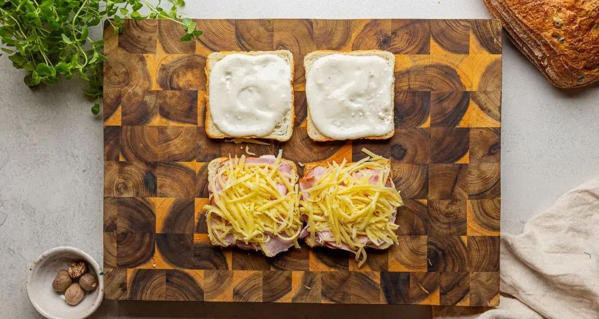 Przygotowanie croque madame: na kromkach chleba szynka i ser, na drugiej sos beszamelowy.