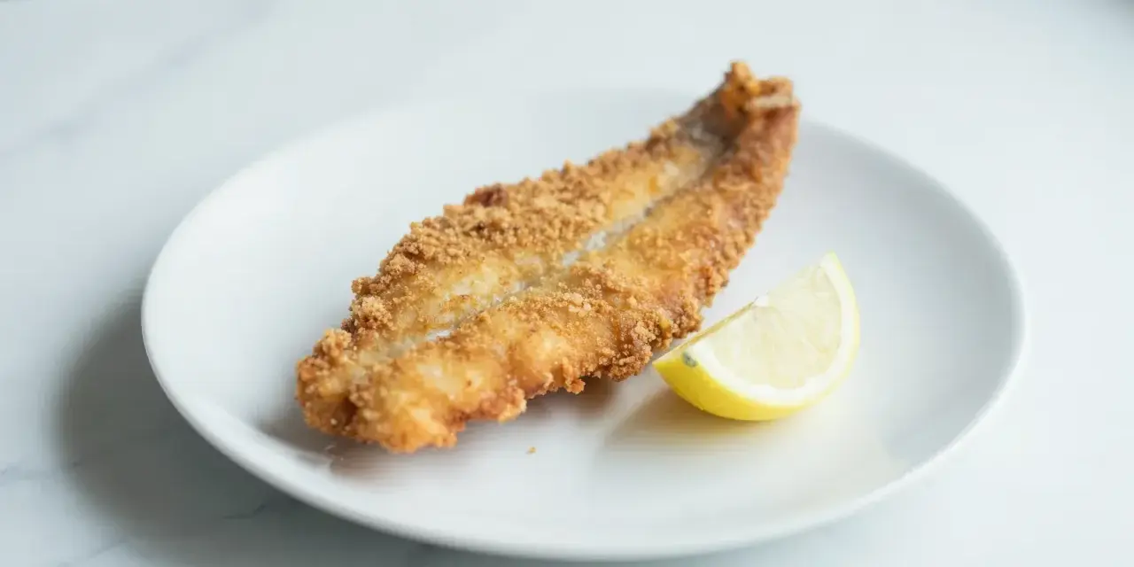 Chrupiący dorsz z airfryer na białym talerzu, z plasterkiem cytryny. Idealny obiad.