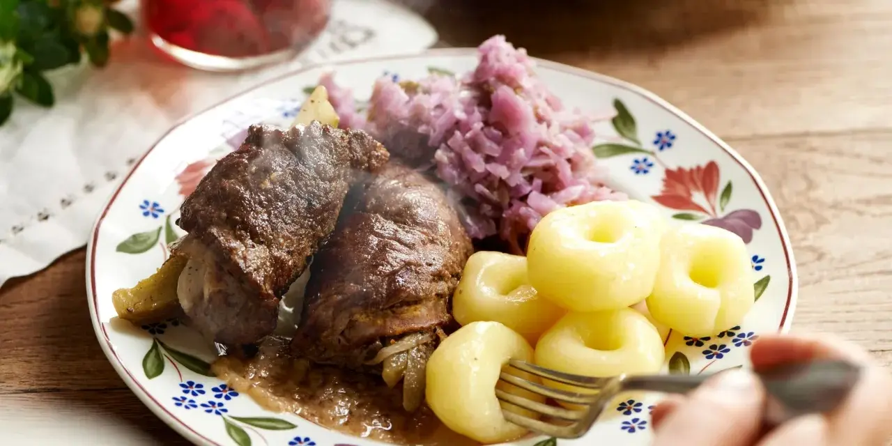 Pyszna rolada śląska z kluskami i czerwoną kapustą, parująca na talerzu.
