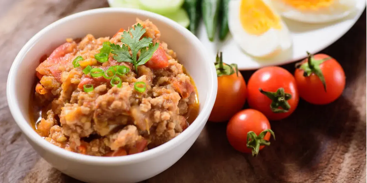 Pyszna pasta z makreli w pomidorach, udekorowana szczypiorkiem i natką. Obok świeże pomidorki i jajka na twardo.