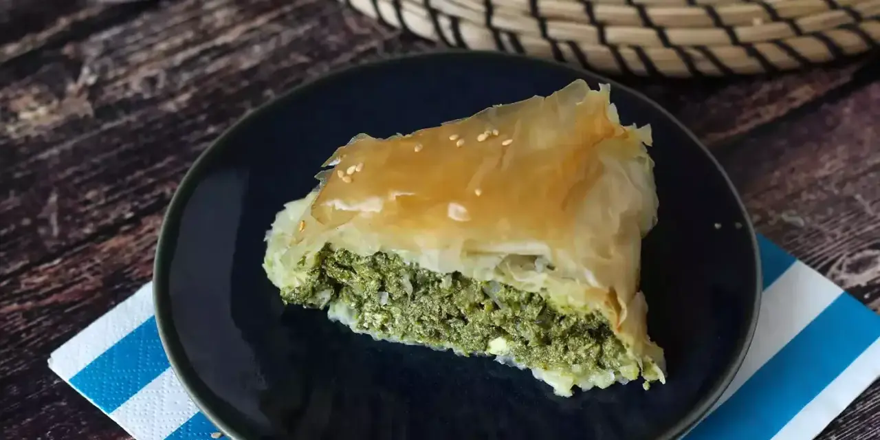 Kawałek spanakopity z chrupiącym ciastem filo i zielonym nadzieniem ze szpinaku i sera feta, posypany sezamem.