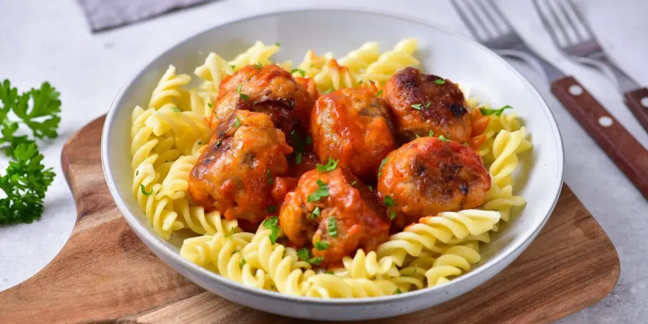 Pulpety w sosie pomidorowym jak u babci, podane z makaronem fusilli. Danie ozdobione posiekaną natką pietruszki.