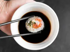 Pałeczkami zanurzam sushi w sosie do sajgonek. Widać kawałek łososia i ryż.