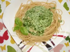 Makaron ze szpinakiem w sosie śmietanowo-serowym, udekorowany listkami bazylii. Pyszne danie na talerzu.