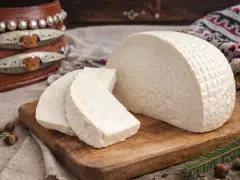 Miękki ser z mleka owczego, pokrojony w trójkąty, leży na desce. Obok orzechy i gałązka świerku.