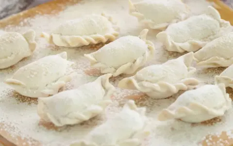 Surowe pierogi, gotowe do gotowania, posypane mąką. Wyglądają jak najlepsze ciasto na pierogi, które mama kiedyś robiła.