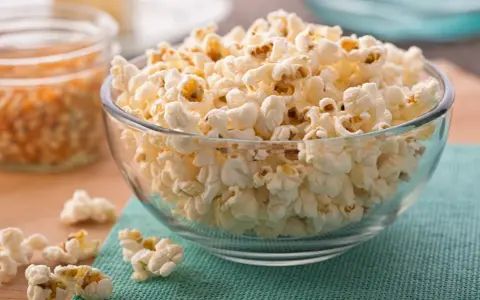 Misternie ułożony popcorn w szklanej misce. Czy popcorn jest zdrowy? To zależy od sposobu przygotowania, ale sam w sobie jest dobrym źródłem błonnika.