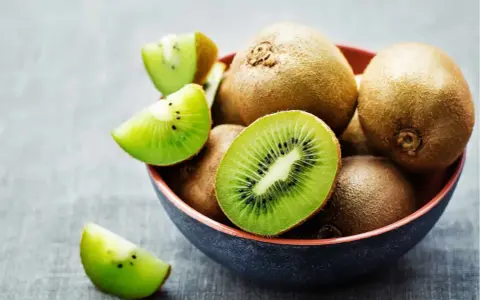 Miseczka pełna kiwi, jedno przekrojone na pół, pokazuje soczysty miąższ. Czy można jeść kiwi ze skórką? Tak, jest jadalna i pełna witamin!
