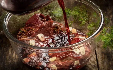 Ciemny płyn wlewa się do szklanej miski z karczkiem, czosnkiem i ziołami. Powstaje aromatyczna marynata do karczku.