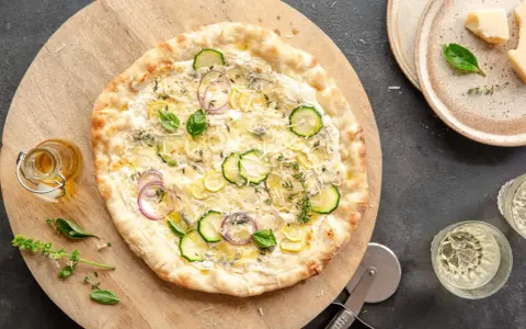 Pyszna pizza bianca z cukinią, cebulą i cytryną, ozdobiona bazylią i tymiankiem. Idealna na letni wieczór.