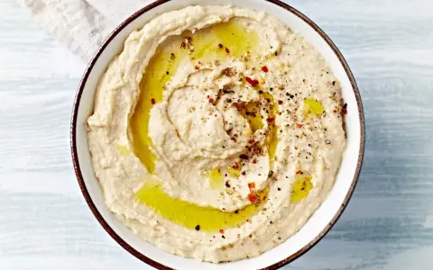 Kremowy, gładki hummus polany oliwą i posypany przyprawami. Idealny do maczania pieczywa.