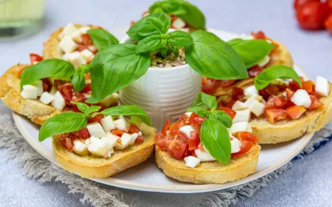 Bruschetta z pomidorami i mozzarellą – pyszny przepis na letnią przekąskę. Chrupiące grzanki z dodatkiem świeżej bazylii.