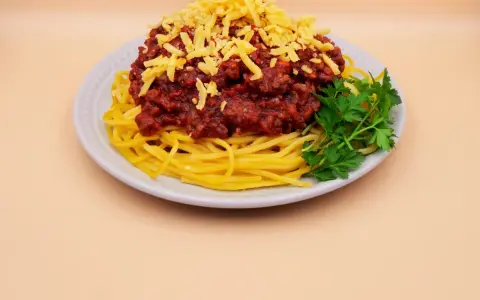 Prosty przepis na spaghetti z mięsem mielonym: makaron, sos boloński, starty ser i natka pietruszki na talerzu.